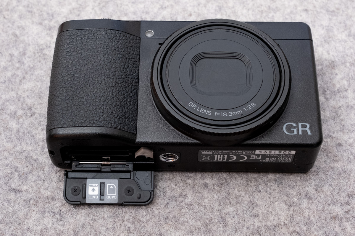 Ricoh GR III camera with battery door open, showing the correct battery door spring position.